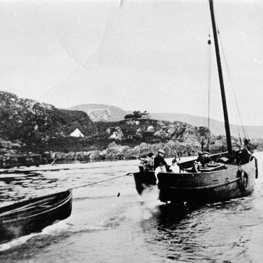 Boat pulling smaller boat out of harbour, Carradale. Engines came into use in the early 1900s. Robert Robertson of Campbeltown installed a 7.9HP Kelving in his 35ft skiff, 'The Brothers'.